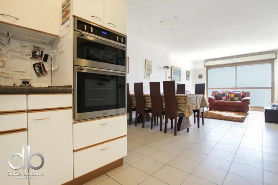Modern Jerusalem real estate apartment with open living and dining area, featuring stylish furniture and ample sunlight, ideal for comfortable city living.