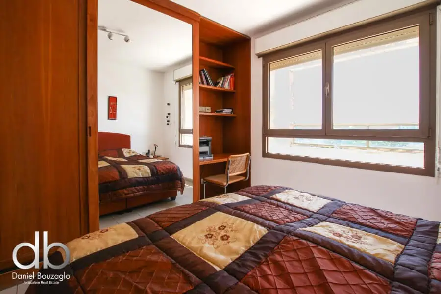 Spacious Jerusalem real estate apartment room with large windows and colorful bedding, ideal for comfortable living and investment.