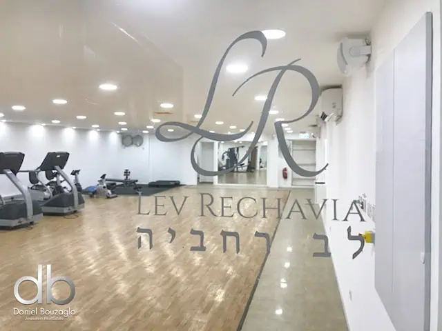 Modern Jerusalem real estate gym interior with fitness equipment, wood flooring, and branding signage for Daniel Bouzaglo.