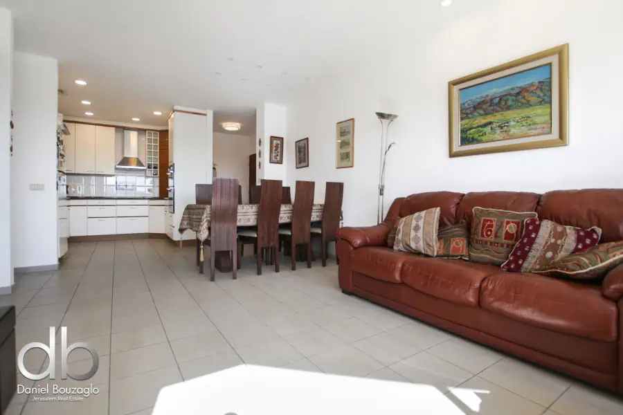 Modern Jerusalem real estate interior with open-concept living and dining area, featuring a comfortable leather sofa, contemporary artwork, and bright natural lighting.