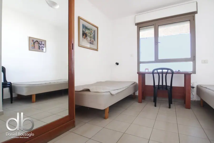 Cozy Jerusalem real estate room with simple furniture and large window, ideal for investment properties or rentals.