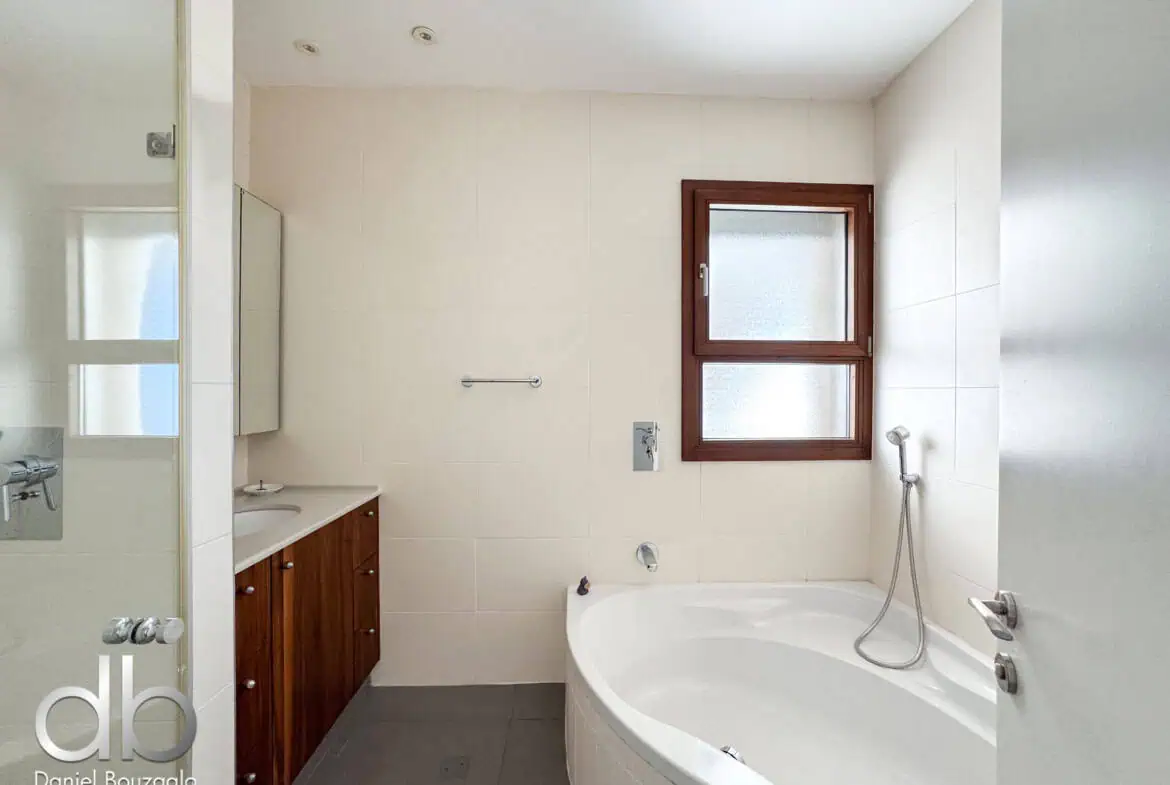 David Crown 25br furnished rental Jerusalem 1 Bright modern Jerusalem bathroom with bathtub and vanity, featuring large window for natural light, sleek fixtures, and neutral tile decor, showcasing premium real estate.