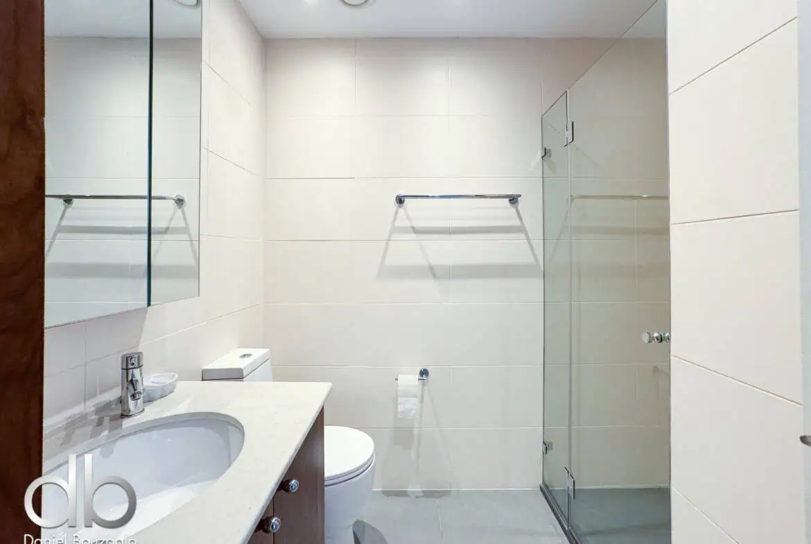 David Crown 25br furnished rental Jerusalem 9 Modern Jerusalem real estate bathroom with white tiled walls and glass shower enclosure, featuring a sleek vanity with marble countertop, showcasing luxurious Jerusalem property details.