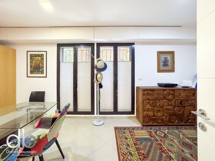 Garden apartment in David VIllage for sale 7 Modern Jerusalem real estate interior with glass dining table, colorful chairs, and wooden alphabet storage cabinet, showcasing contemporary Jerusalem property design.