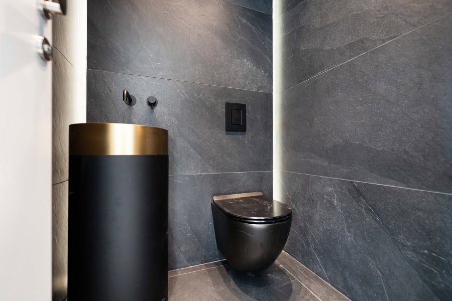 Harakevet rd duplex penthouse for sale 10_1 Modern Jerusalem real estate bathroom with sleek black toilet and matching black sink with gold accent, housed in a stylish grey stone-tiled space.