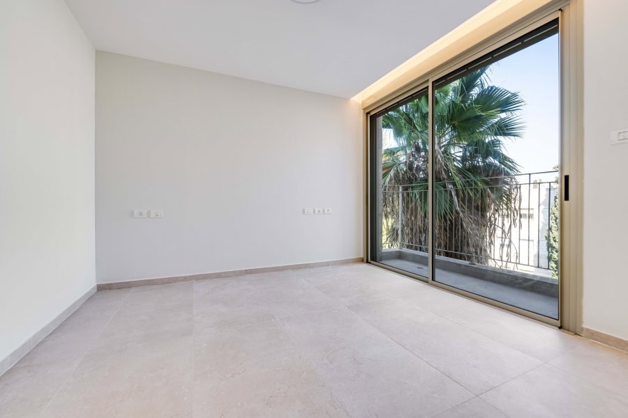 Harakevet rd duplex penthouse for sale 3_1 Modern Jerusalem real estate interior with large glass sliding doors and balcony view of lush palm trees, bright natural lighting, and minimalist design for luxury living.