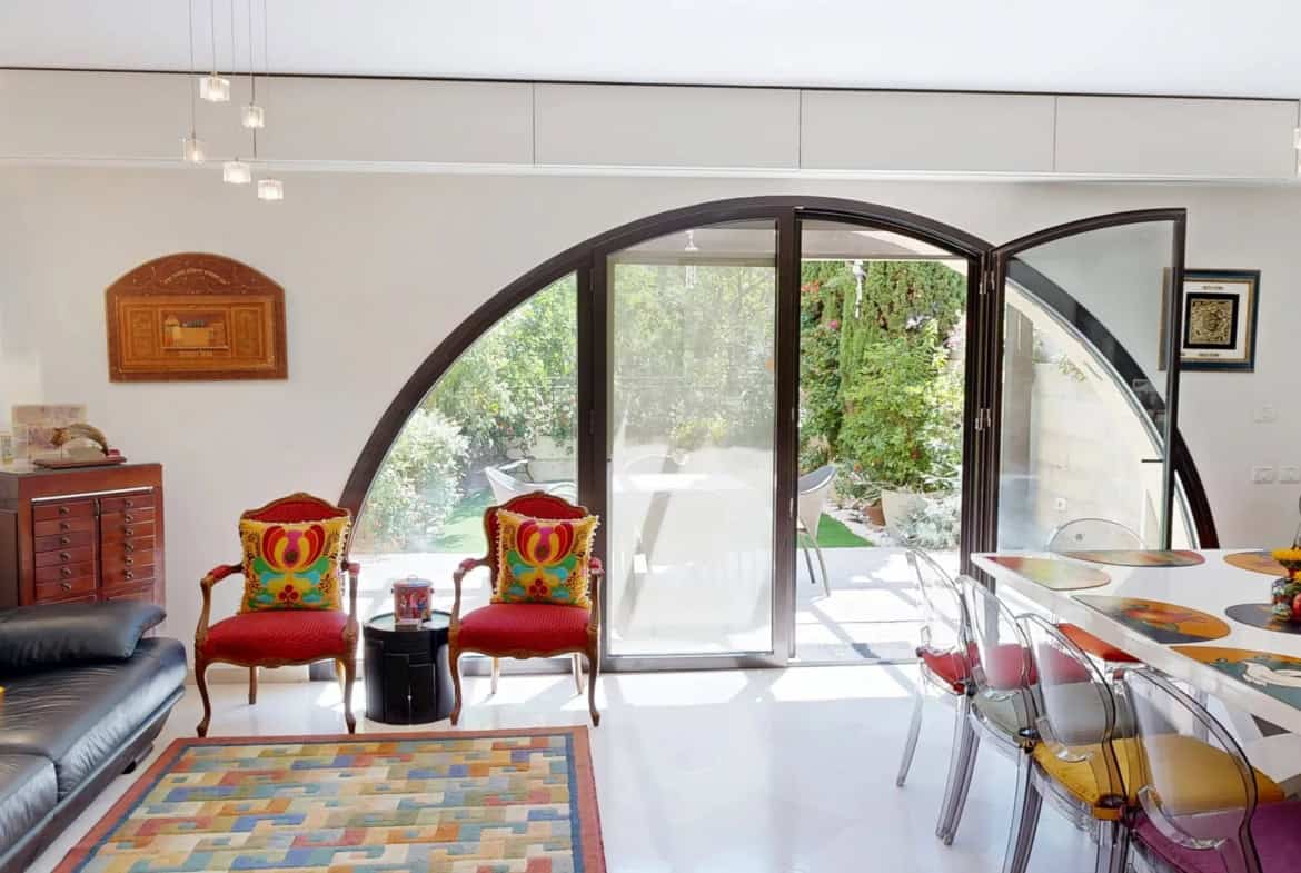 Ismach Melech David VIllage town house 4 Contemporary Jerusalem living room with large curved glass doors leading to lush outdoor garden, stylish furniture, colorful decor, and natural light, showcasing Jerusalem real estate by Daniel Bouzaglo.