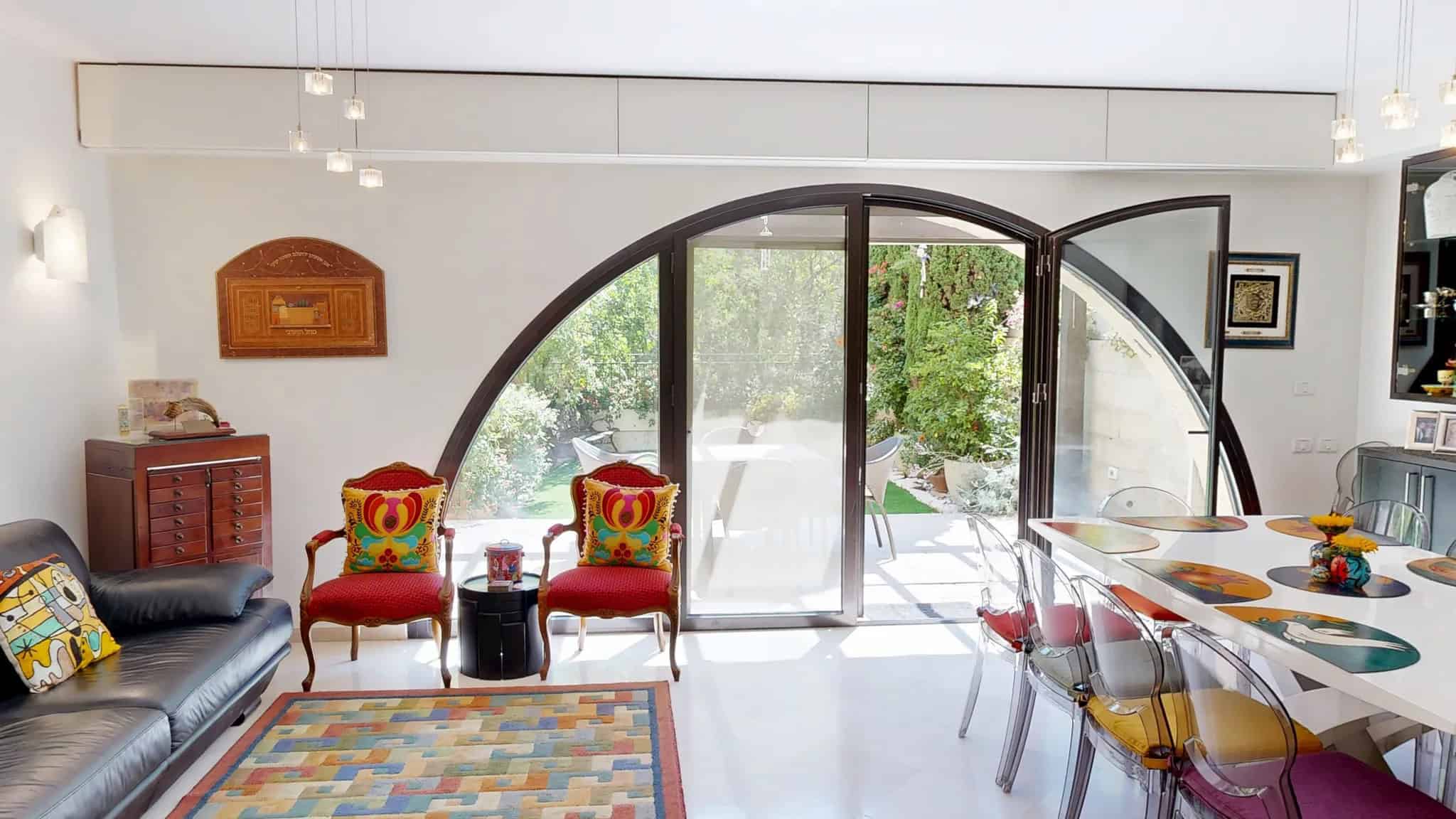 Ismach Melech David VIllage town house 4 Contemporary Jerusalem living room with large curved glass doors leading to lush outdoor garden, stylish furniture, colorful decor, and natural light, showcasing Jerusalem real estate by Daniel Bouzaglo.