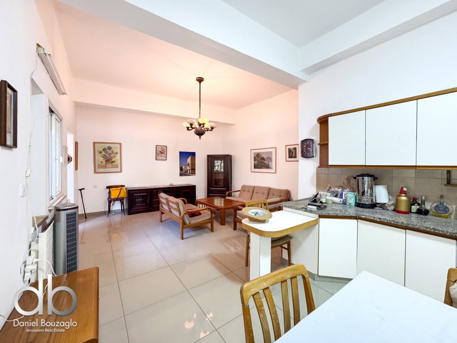 Bright Jerusalem real estate living room with white walls, wooden furniture, and modern kitchen appliances, showcasing a cozy and spacious interior.