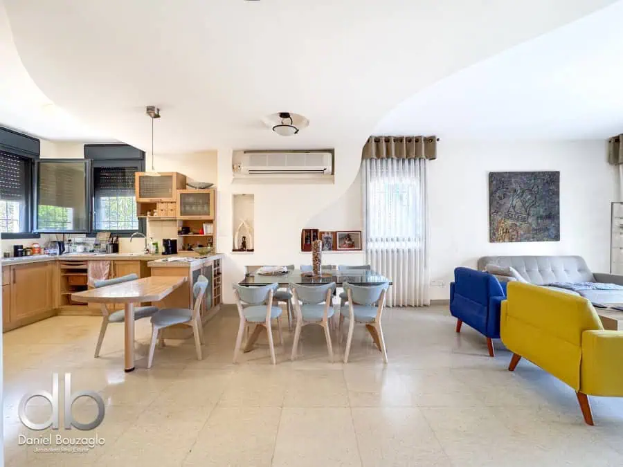 Bright and airy Jerusalem real estate interior with open-plan kitchen, dining area, and modern living room featuring colorful chairs and decorative artwork.