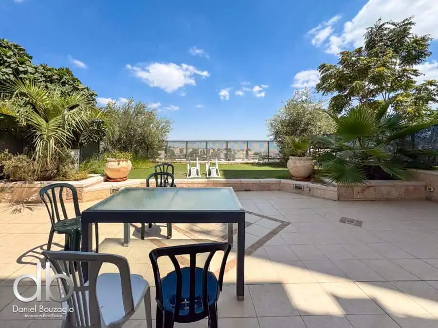 Balcony with outdoor seating, lush greenery, and panoramic Jerusalem city views, ideal for real estate showcasing in Jerusalem.