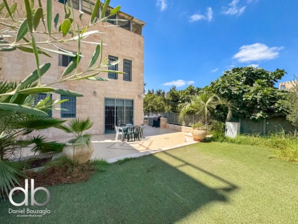 Spacious outdoor patio area at Jerusalem real estate property with lush greenery and modern outdoor furniture under blue skies.