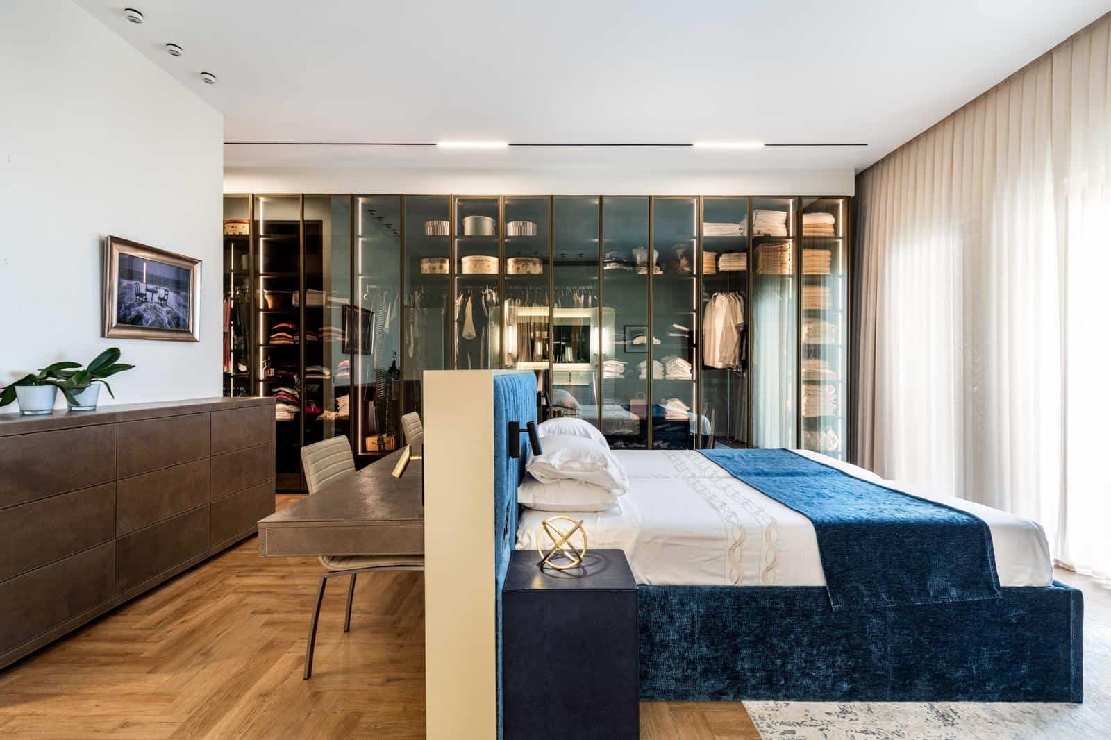 Luxury Jerusalem real estate bedroom with modern design and spacious closet area. Stunning bedroom in Jerusalem real estate featuring a sleek, modern design, a stylish closet with glass doors, and abundant natural light, perfect for a luxurious living experience.