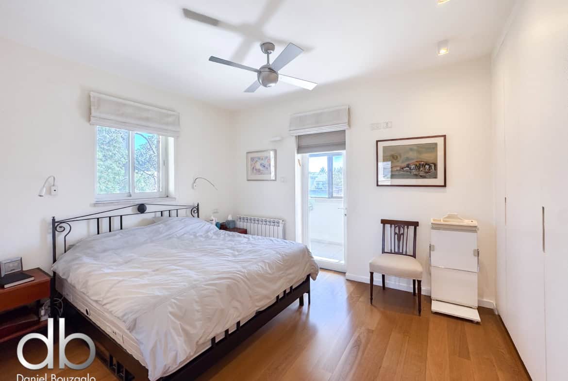 Bright bedroom with white walls, a black metal bed frame, white bedding, a ceiling fan, and two windows with blinds nearby.