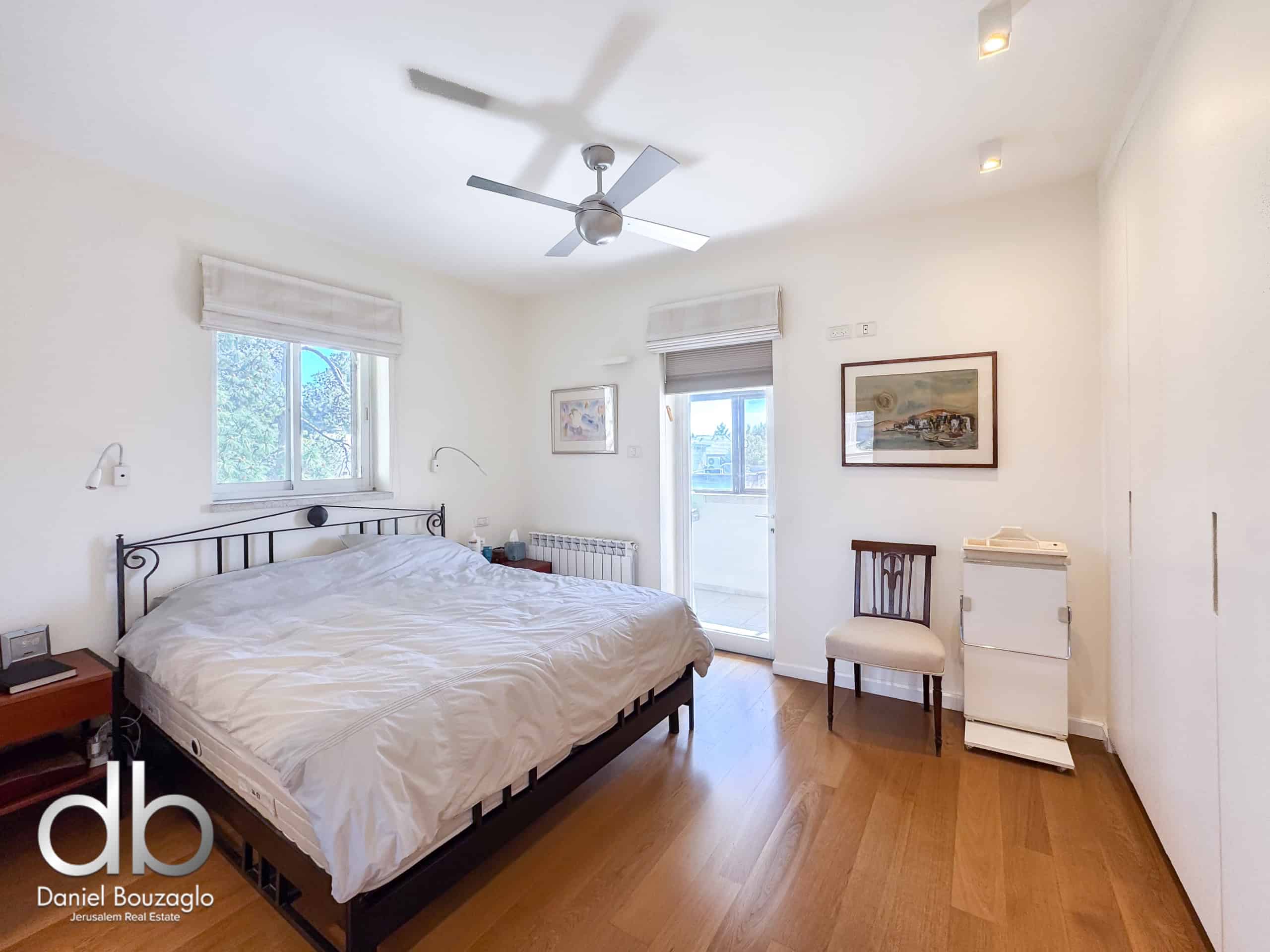 Bright bedroom with white walls, a black metal bed frame, white bedding, a ceiling fan, and two windows with blinds nearby.