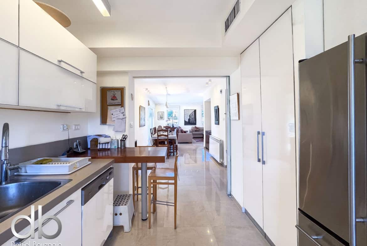 Bright modern kitchen with white glossy cabinets, a stainless steel refrigerator, and a view through to a dining area in the living room. Open-plan kitchen-dining space with an island and wooden chairs.