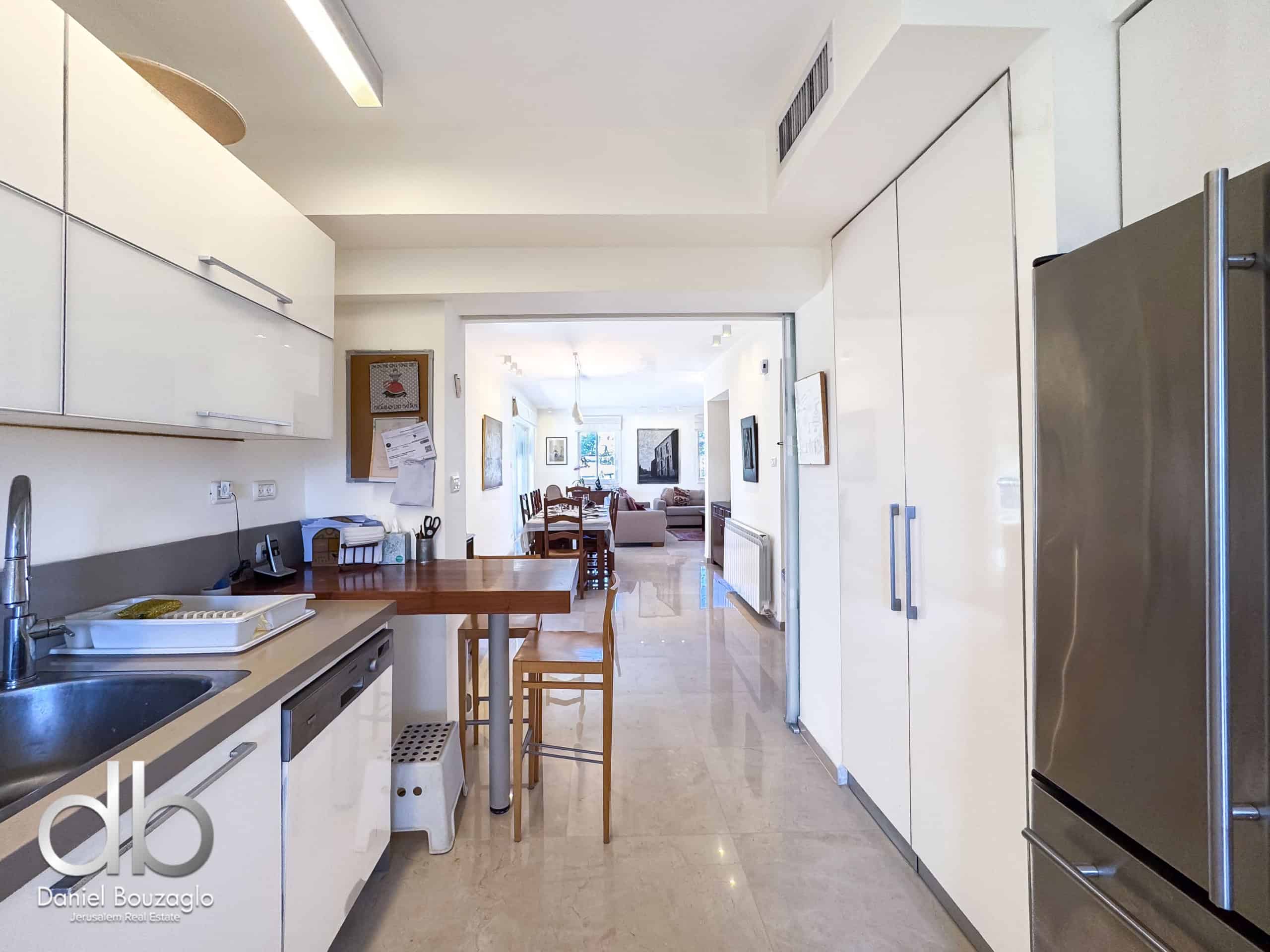 Bright modern kitchen with white glossy cabinets, a stainless steel refrigerator, and a view through to a dining area in the living room. Open-plan kitchen-dining space with an island and wooden chairs.