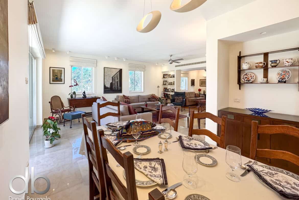 Bright open-plan dining room with a long table set for dinner, glasses and plates, and a living area in the background.