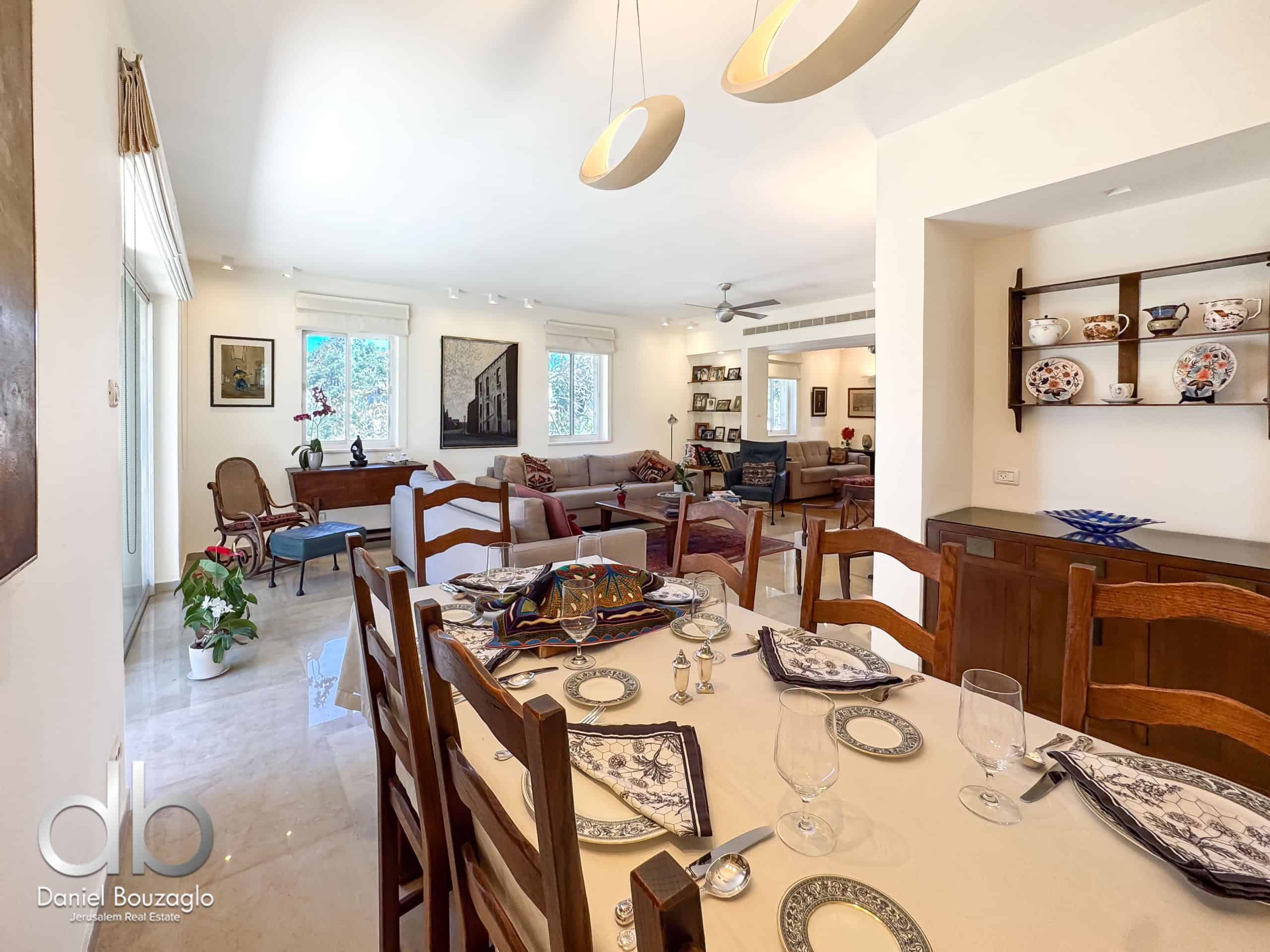 Bright open-plan dining room with a long table set for dinner, glasses and plates, and a living area in the background.