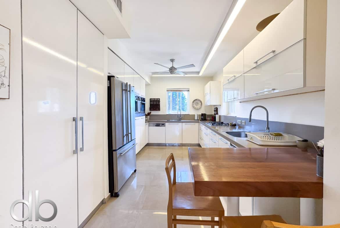 Modern bright kitchen with white cabinets, stainless steel appliances, and a wooden dining table in the foreground.