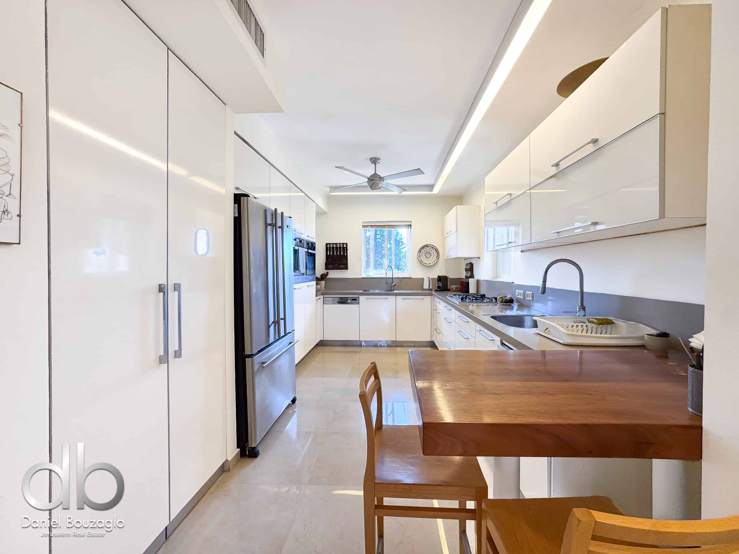Modern bright kitchen with white cabinets, stainless steel appliances, and a wooden dining table in the foreground.