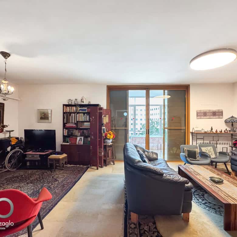 Spacious living room with black leather sofas, a wooden coffee table, rugs, and a large glass door to a balcony, bright natural light.