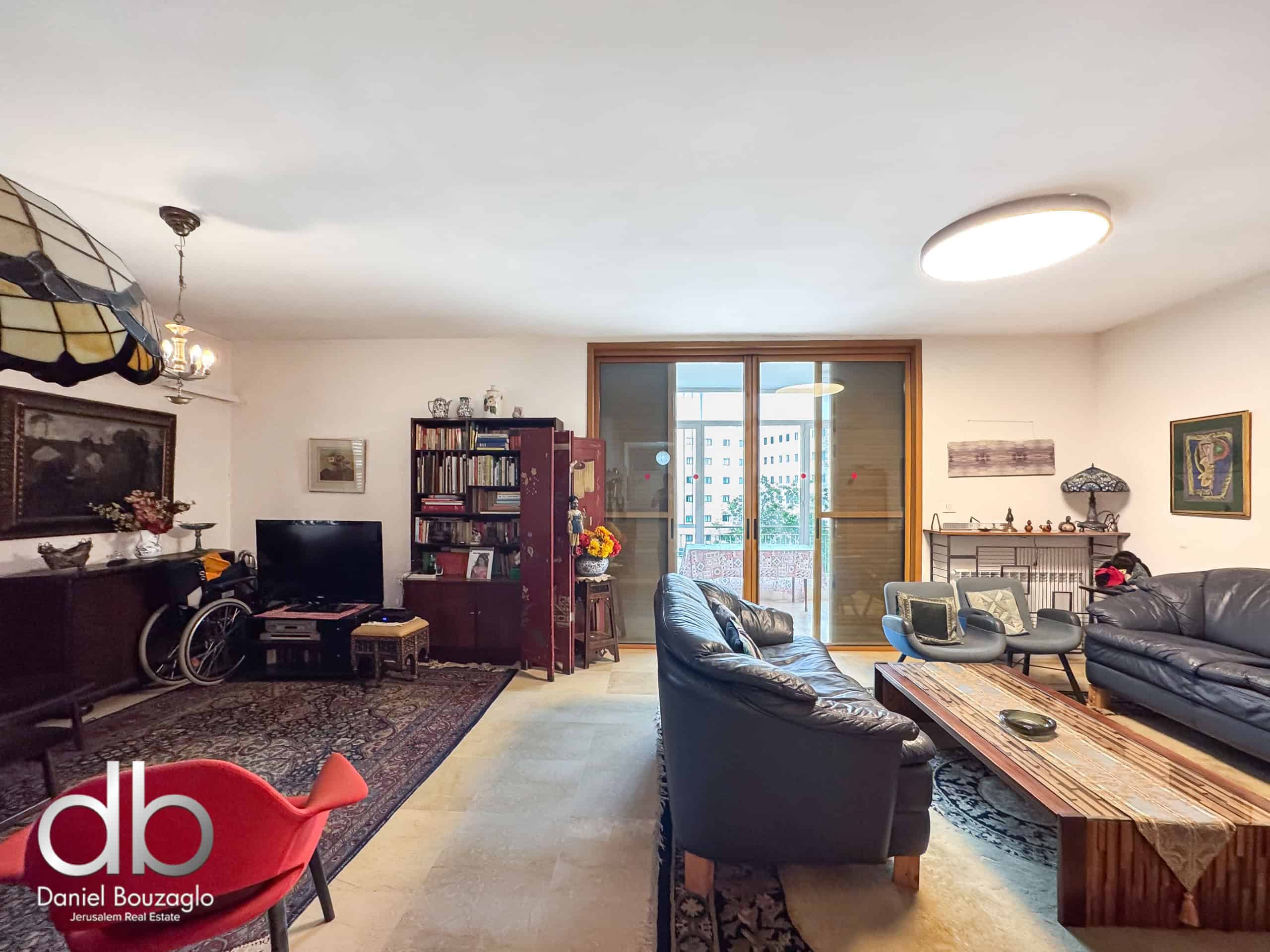 Spacious living room with black leather sofas, a wooden coffee table, rugs, and a large glass door to a balcony, bright natural light.