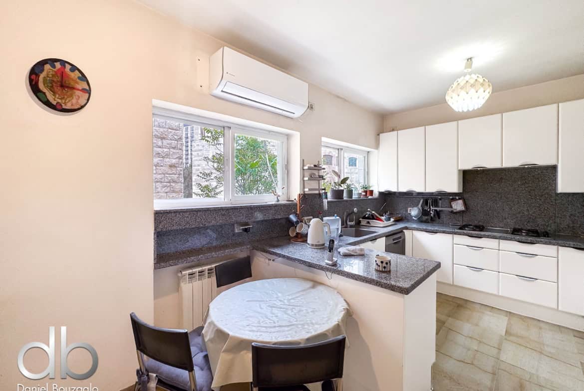 Bright kitchen with white cabinets, granite countertops, and a round table covered with a tablecloth and four black chairs nearby.