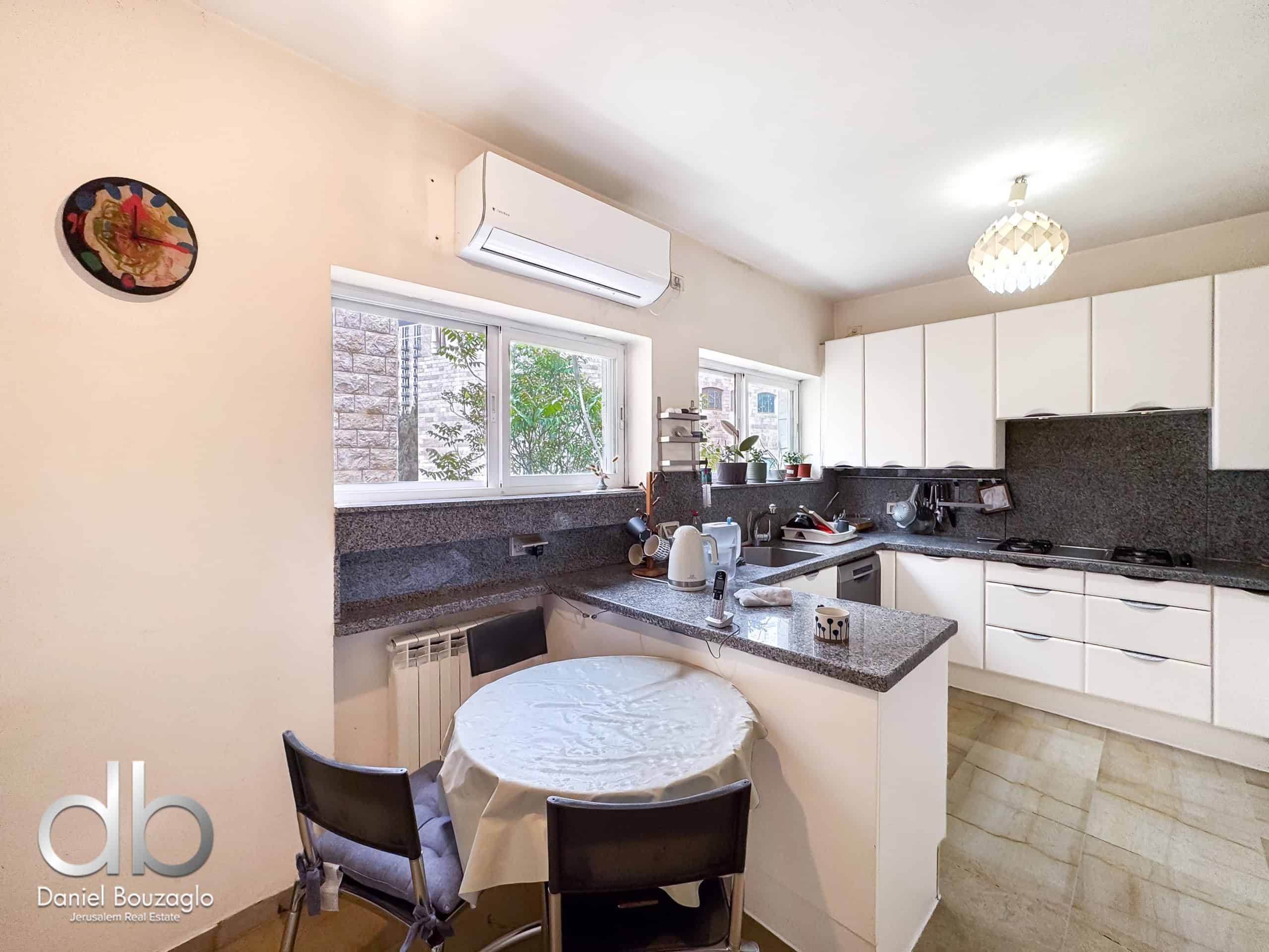 Bright kitchen with white cabinets, granite countertops, and a round table covered with a tablecloth and four black chairs nearby.