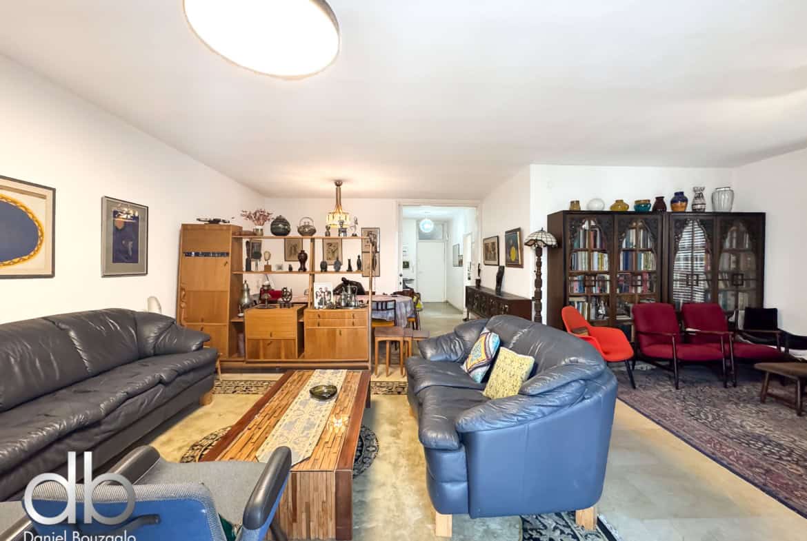 Spacious living room with blue leather sofas, wooden shelves, and a tall display cabinet filled with decorative items on the right.