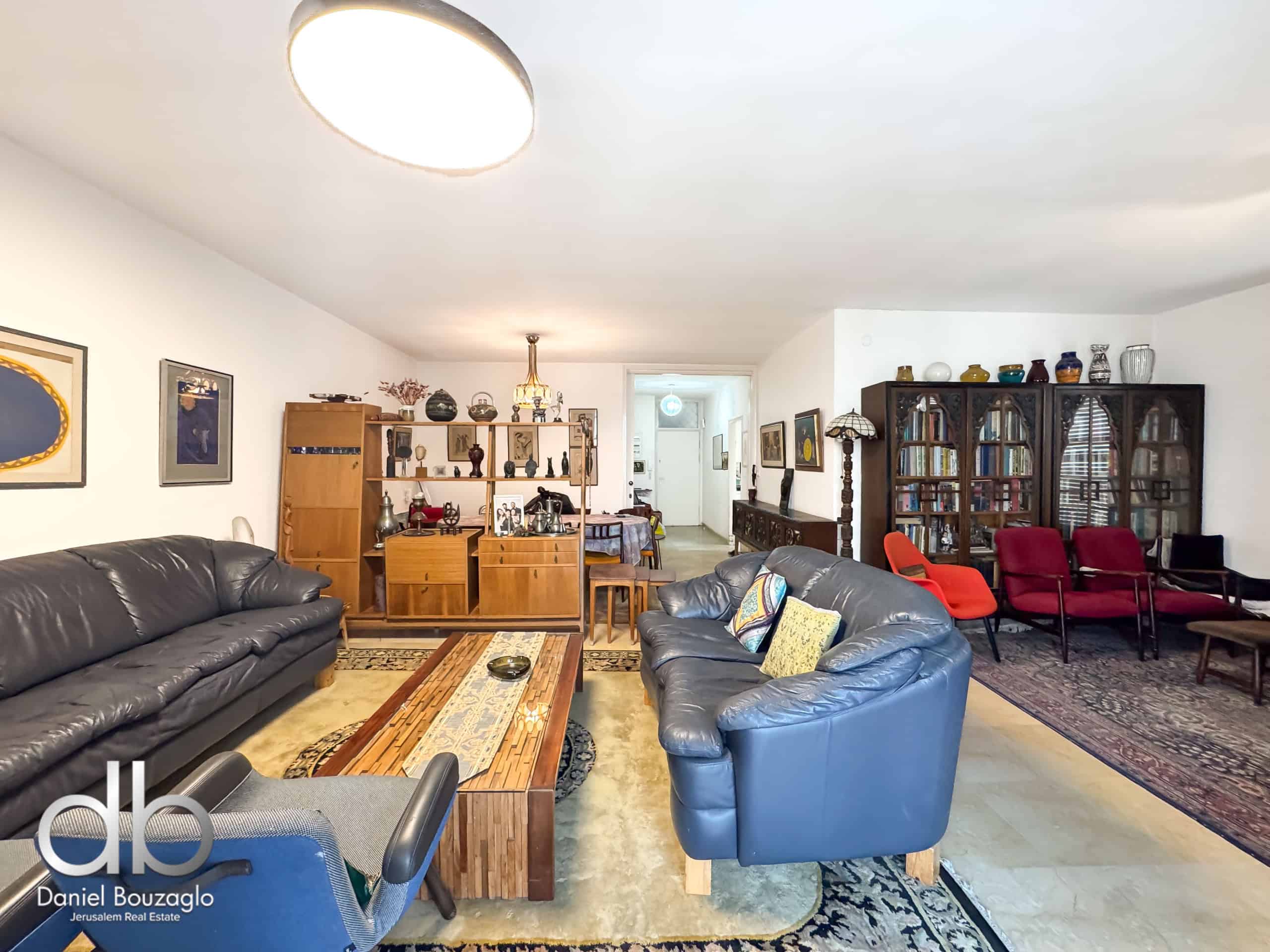 Spacious living room with blue leather sofas, wooden shelves, and a tall display cabinet filled with decorative items on the right.