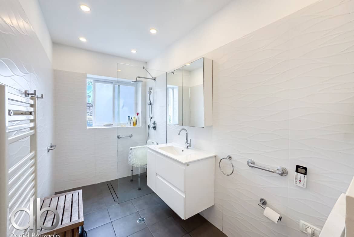 Bright, modern bathroom with a glass shower enclosure, white vanity, and textured white wall tiles.