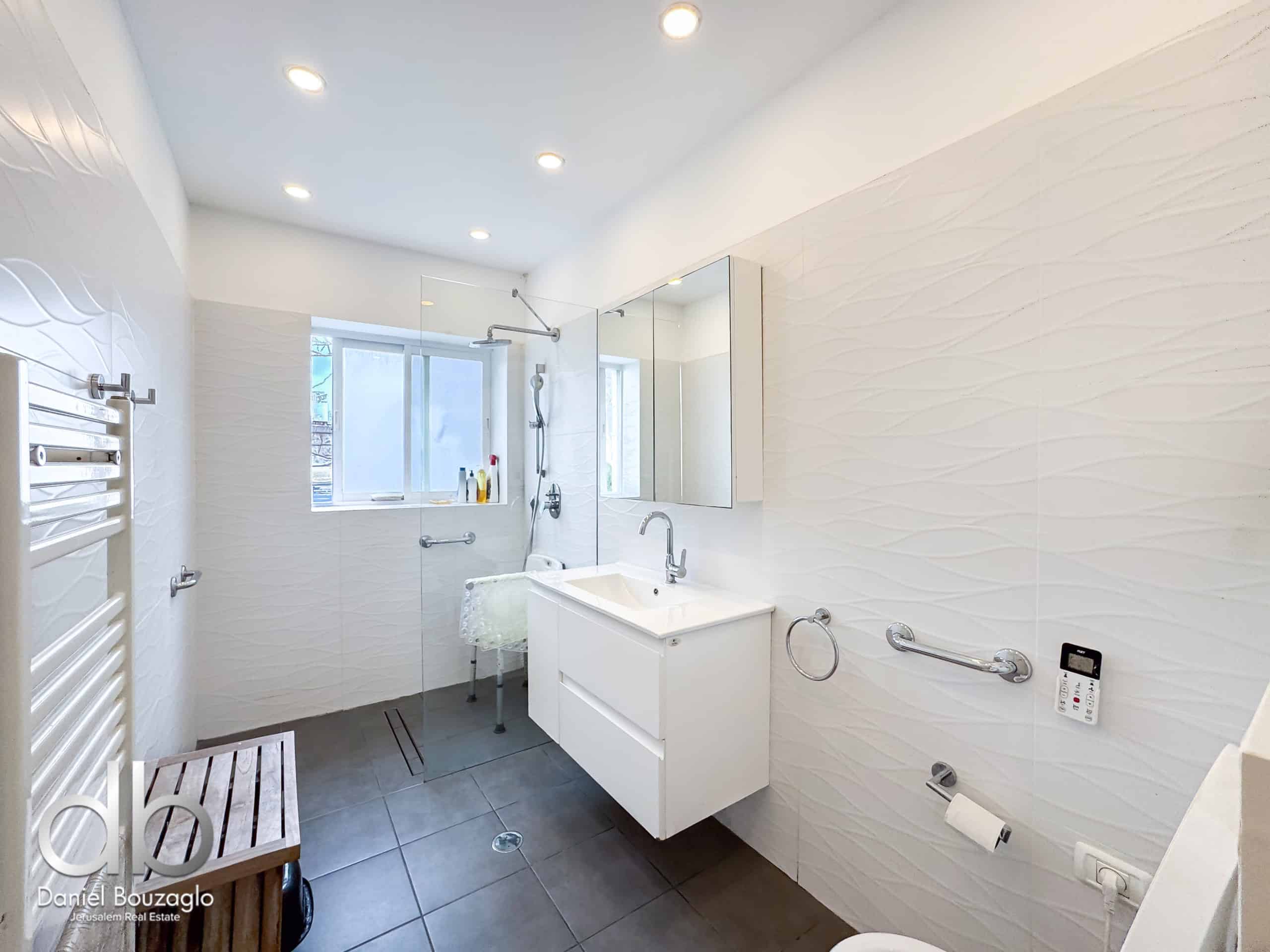 Bright, modern bathroom with a glass shower enclosure, white vanity, and textured white wall tiles.