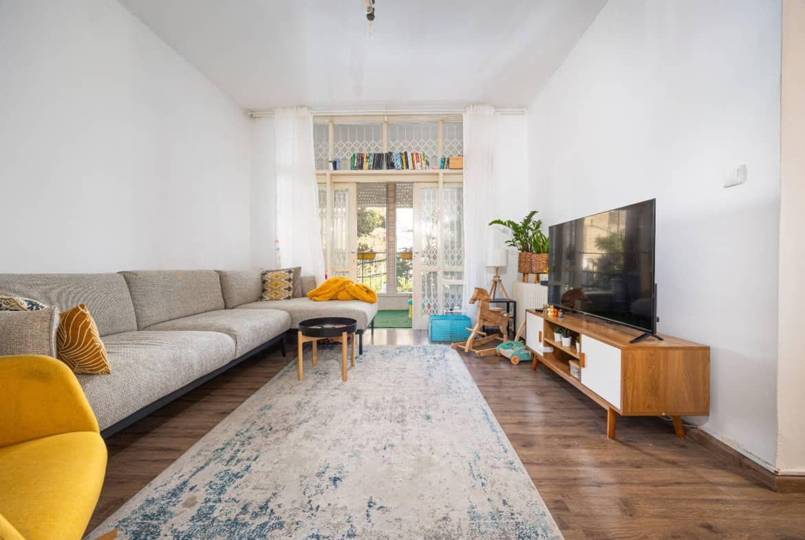 Bright living room with a grey sectional sofa, yellow chair, and a wooden TV console facing a large flat-screen TV.