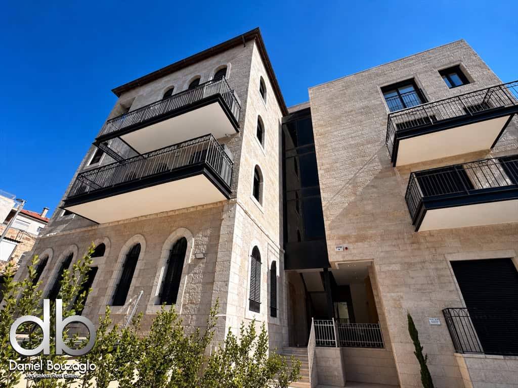 Modern stone apartment building with multiple black metal balconies against a clear blue sky; logo 'db' bottom left.