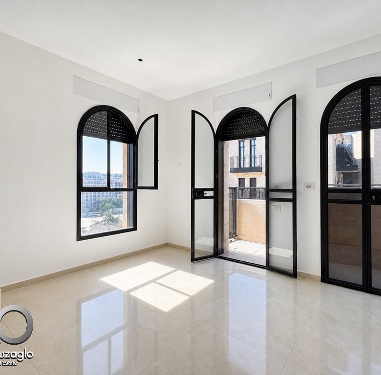 Bright empty room with large black arched windows and a balcony door, white walls, and glossy beige tile floor.