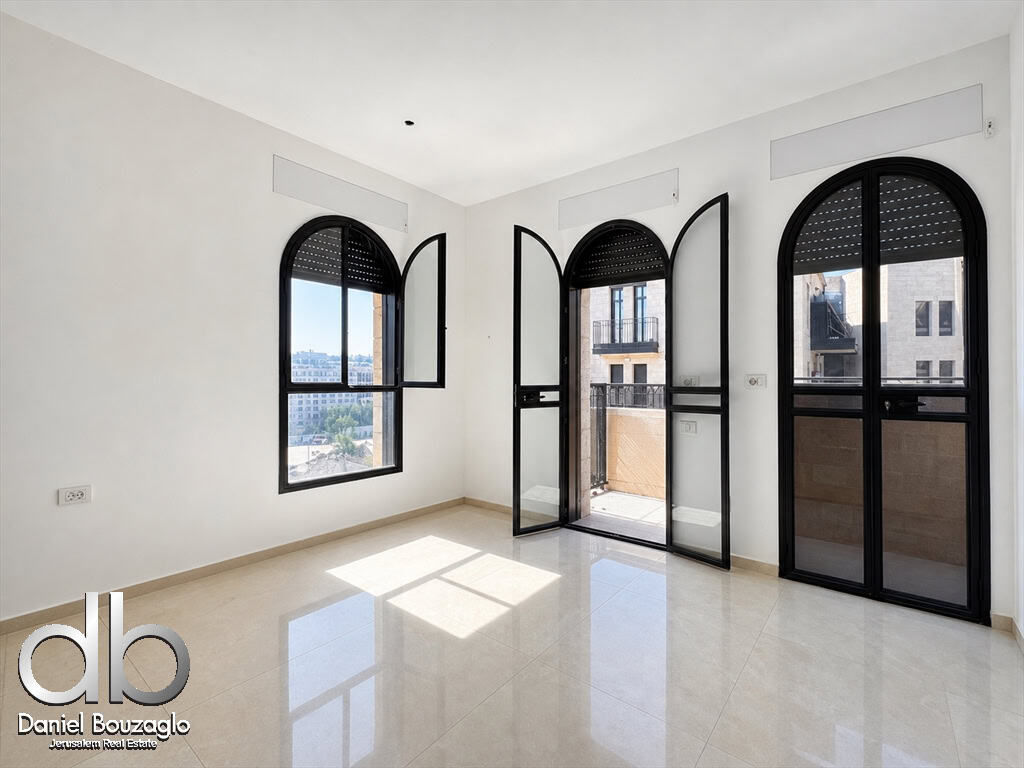 Bright empty room with large black arched windows and a balcony door, white walls, and glossy beige tile floor.