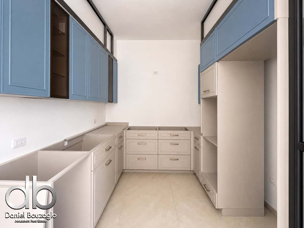 Contemporary kitchen with blue upper cabinets, white base cabinets, and a large L-shaped counter, bright and airy.