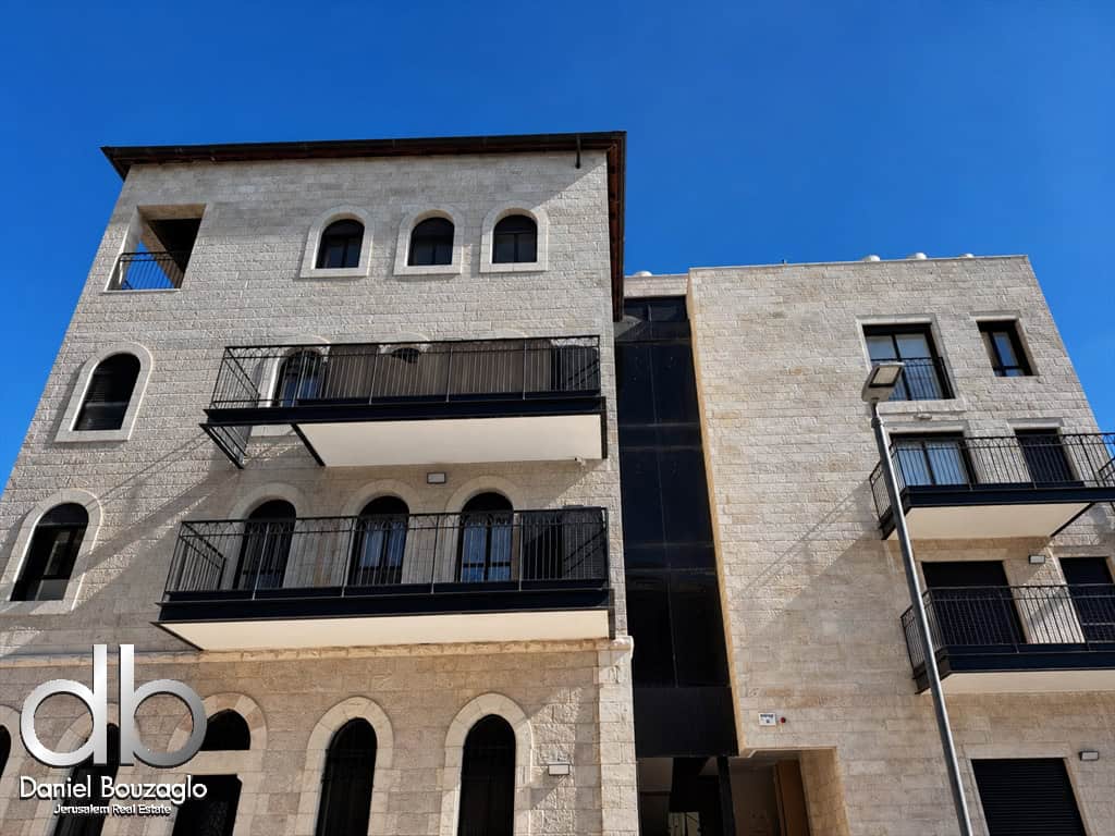 Contemporary stone apartment building with multiple balconies and arched windows under a blue sky.