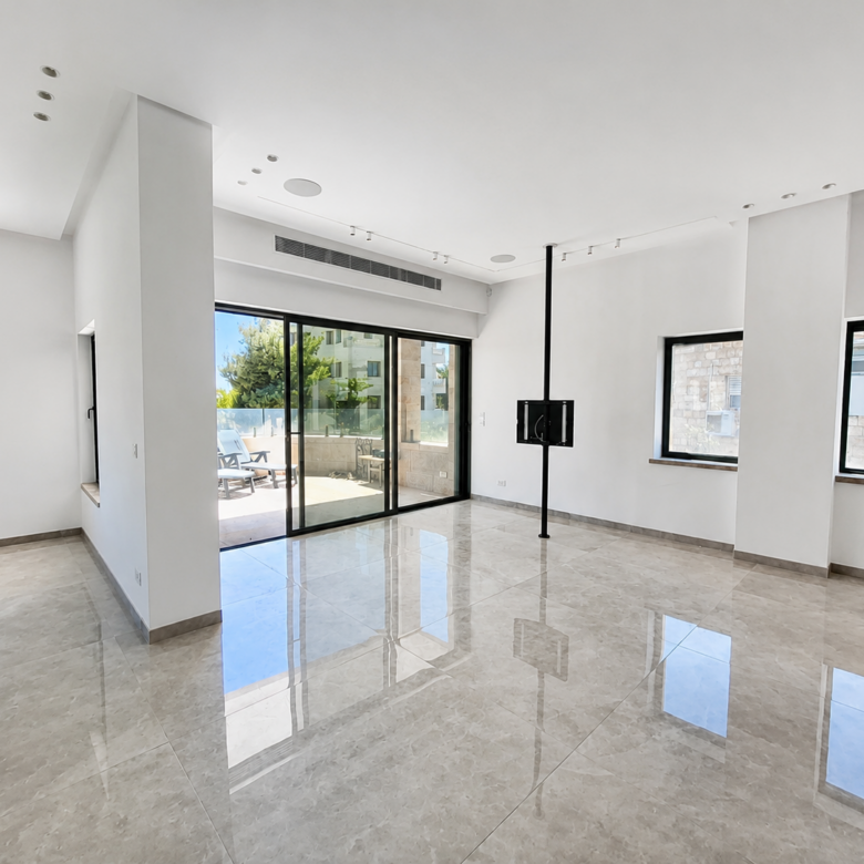 Bright empty living room with glossy tile floor, white walls, and large sliding glass doors to a sunny patio outside