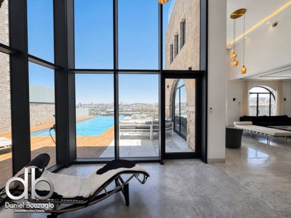 Luxurious open-plan living area with floor-to-ceiling glass walls, a pool deck outside, and modern lounge furniture.