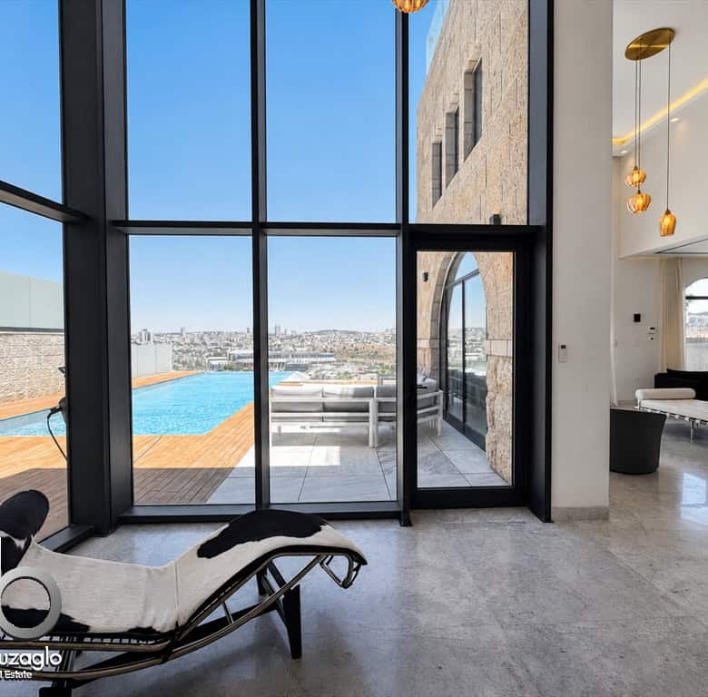 Luxurious open-plan living area with floor-to-ceiling glass walls, a pool deck outside, and modern lounge furniture.