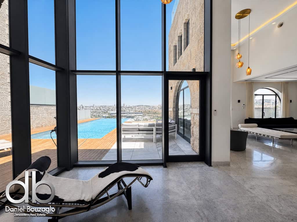 Luxurious open-plan living area with floor-to-ceiling glass walls, a pool deck outside, and modern lounge furniture.