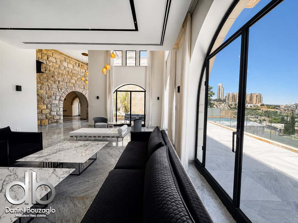 Luxurious living room with marble floors, a stone wall with an arched opening, black sofa, and floor-to-ceiling windows overlooking a city skyline.