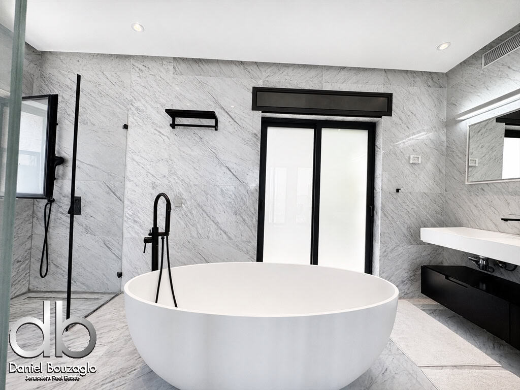 Modern marble bathroom with a freestanding white tub, glass shower, and black fixtures. Sliding frosted doors in the back.