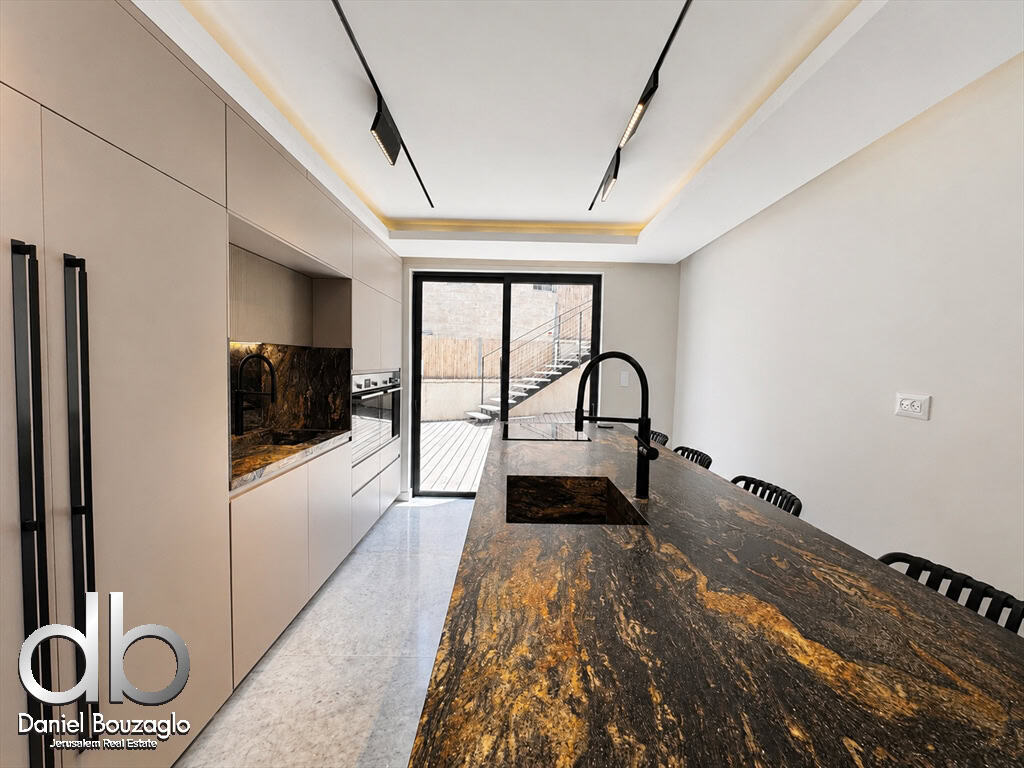 Modern kitchen with a long dark marble island, black gooseneck sink, beige cabinets, and a glass sliding door to a wooden deck.