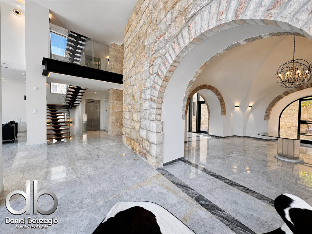 Spacious modern lobby with arched stone walls, marble floor, and a floating glass-railed staircase.
