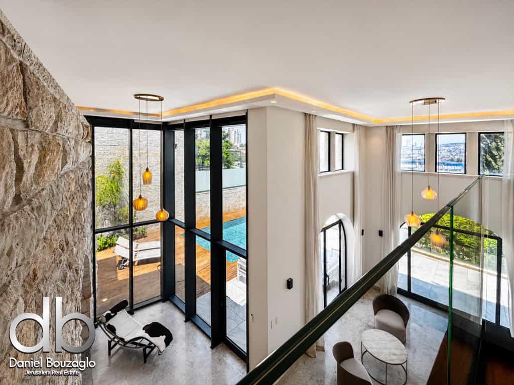 Open two-story living area with floor-to-ceiling windows, stone accent wall, and a pool visible outside.