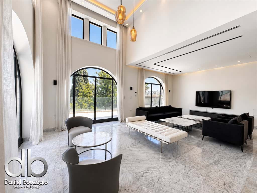 Bright, modern living room with marble floors, large arched windows/doors, white drapes, and black sofas facing a wall-mounted TV.