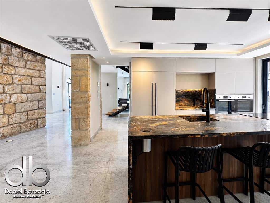 Modern kitchen with a dark marble island, black sink faucet, white cabinets, and built‑in ovens; stone accent wall on the left.